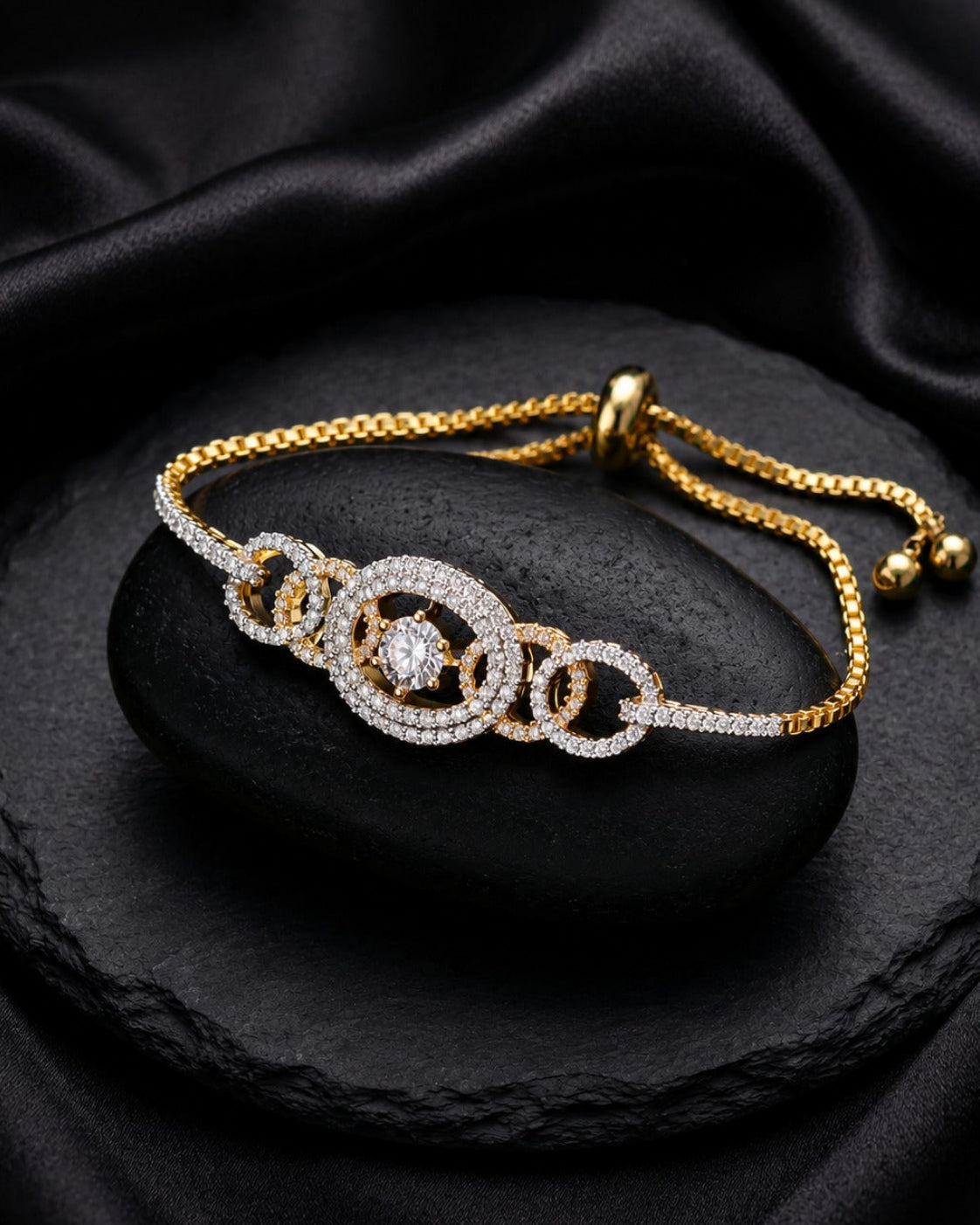 A gold and white stone bracelet with interlocking circular links, displayed on a black stone slab with draped black satin fabric in the background.