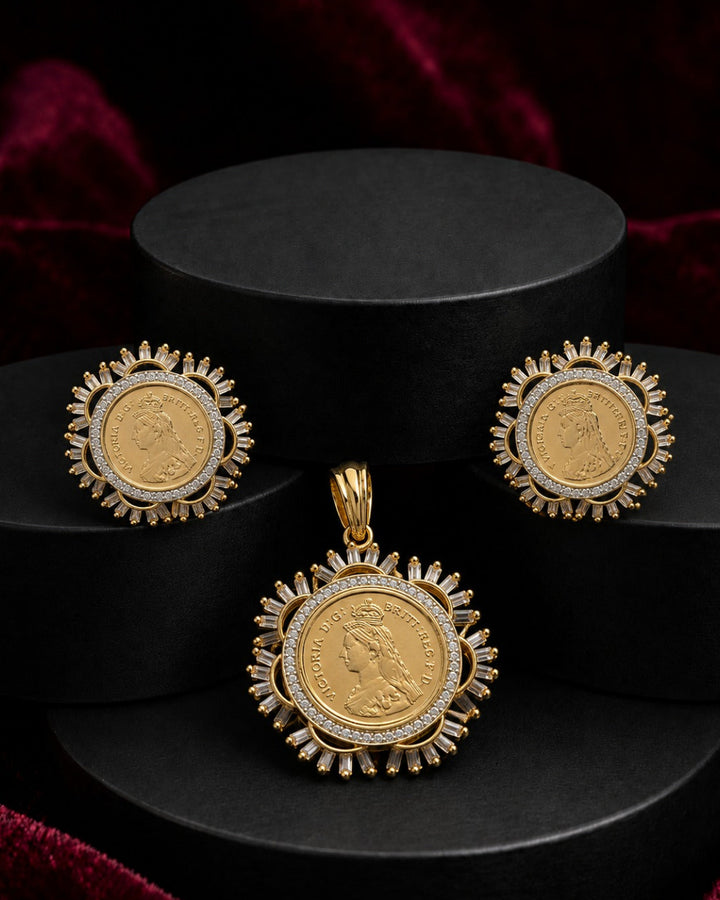 A gold coin jewelry set featuring a pendant and matching earrings, displayed on black cylindrical pedestals against a dark red velvet background.