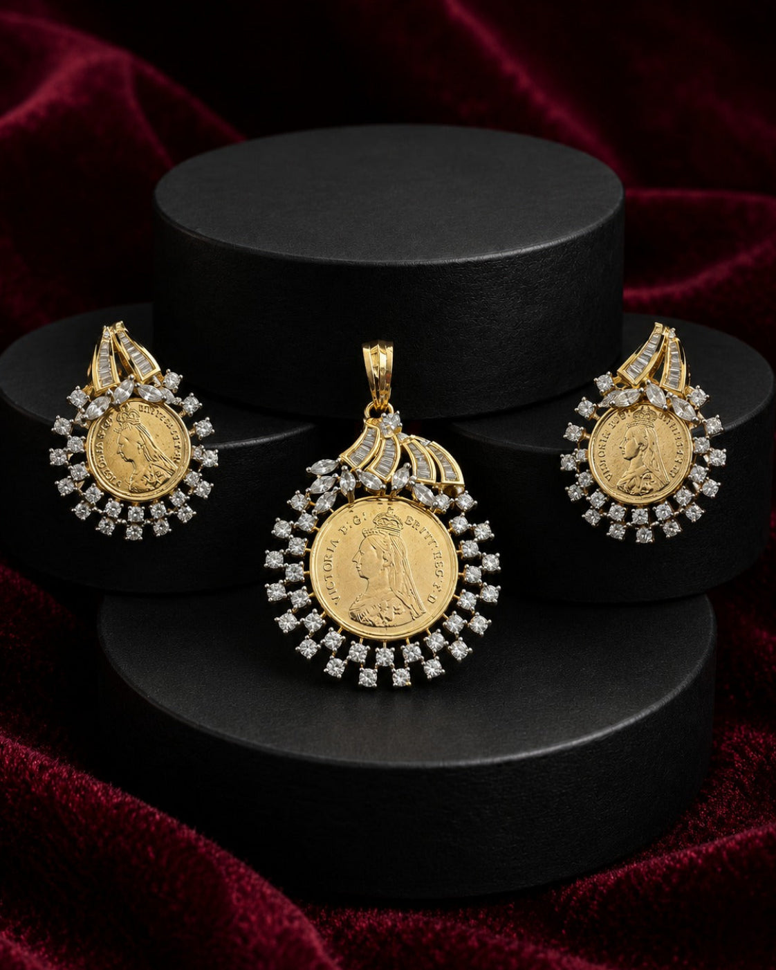 A gold coin pendant necklace with diamond accents, displayed alongside matching earrings on black cylindrical pedestals against a dark red velvet background.