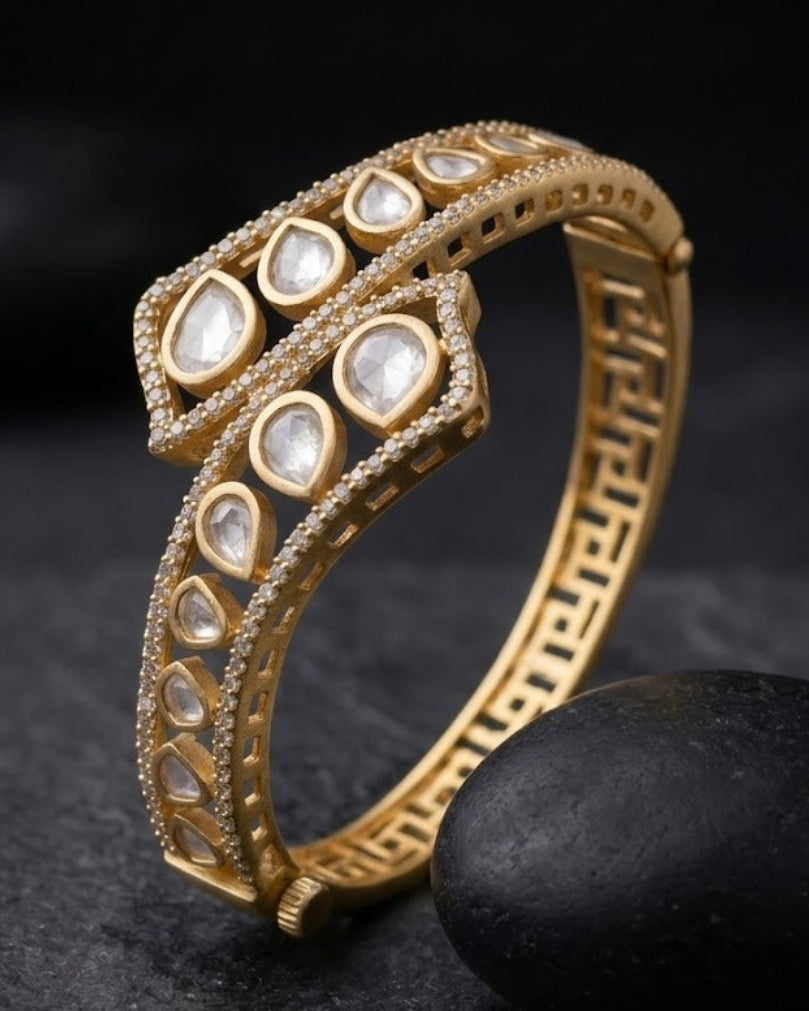 A gold snake-shaped ring adorned with clear kundan stones, displayed on a dark textured surface next to a black stone.