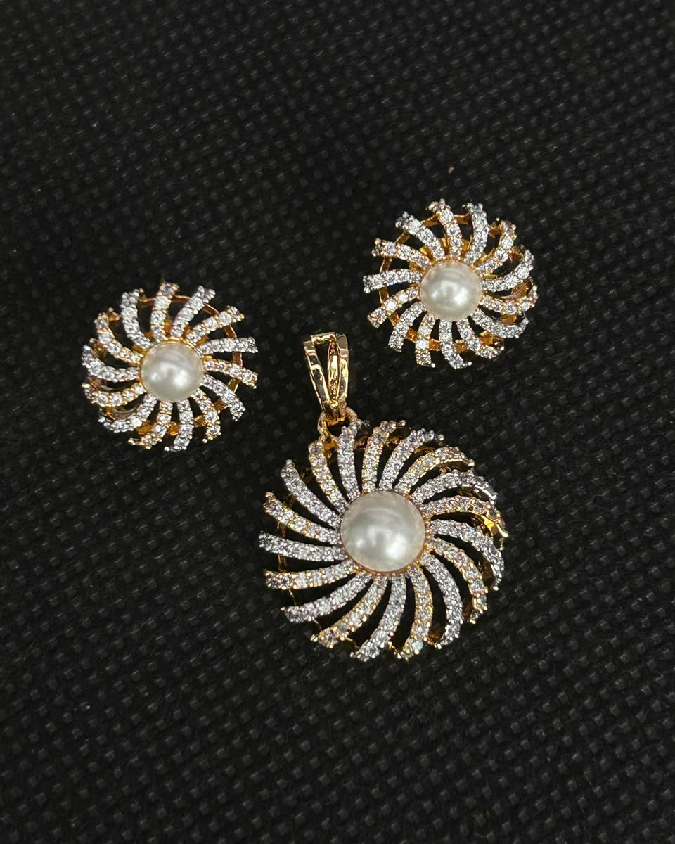 A gold-tone jewelry set featuring a matching pendant and earring, both with a spiral sunburst design set with clear rhinestones and a central white pearl, displayed on a textured black background.