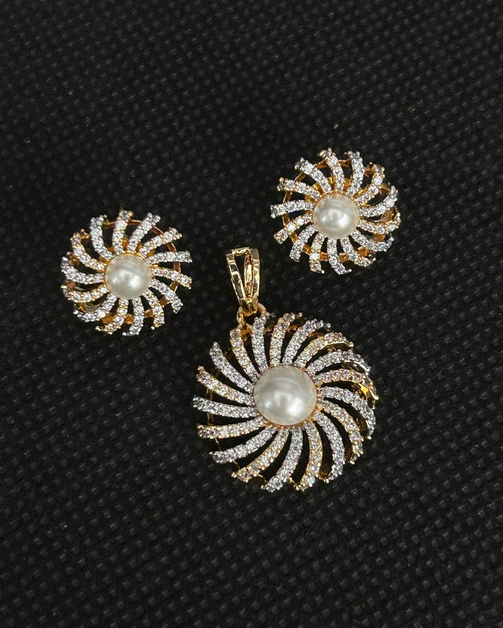 A gold-tone jewelry set featuring a matching pendant and earring, both with a spiral sunburst design set with clear rhinestones and a central white pearl, displayed on a textured black background.