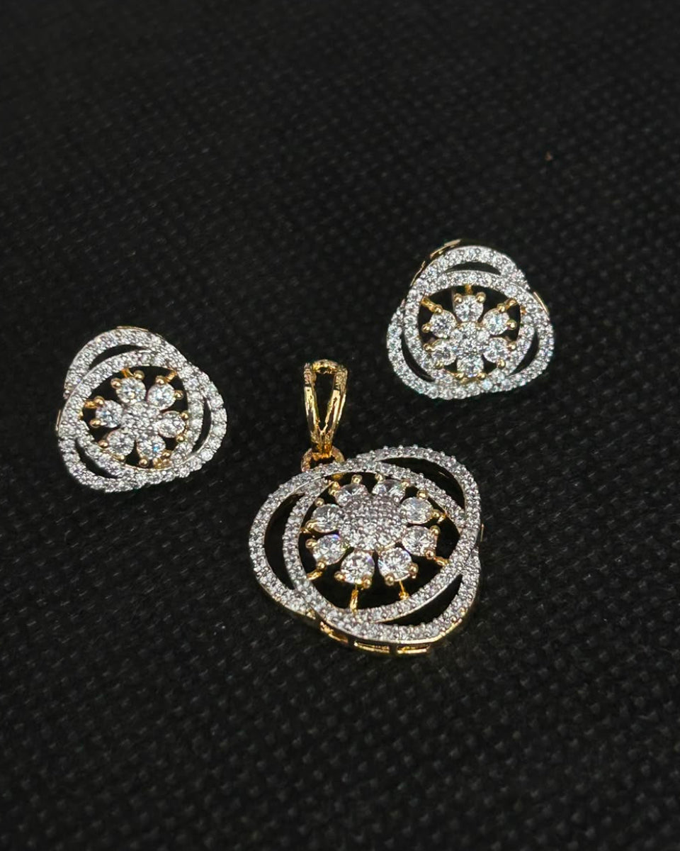 A gold and silver-tone jewelry set featuring a matching pendant and stud earrings with a circular, floral pavé design, displayed on a textured black background.