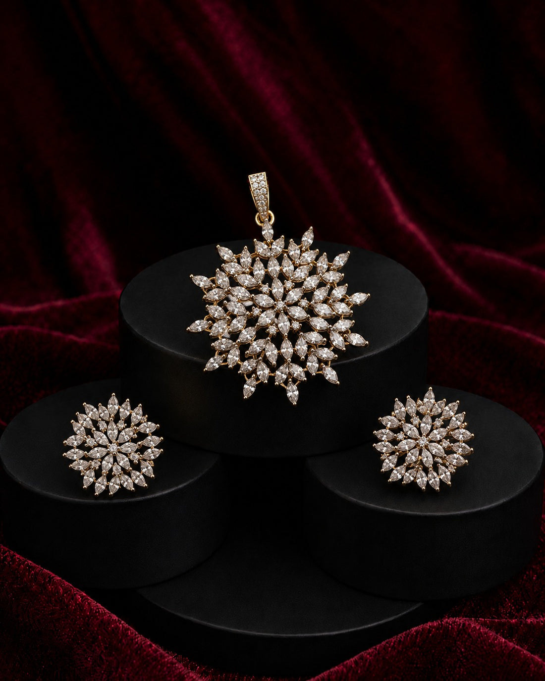 A jewelry set featuring a snowflake-shaped pendant, matching earrings, and a ring, all set in yellow gold and adorned with clear stones, displayed on black pedestals against a dark red velvet background.
