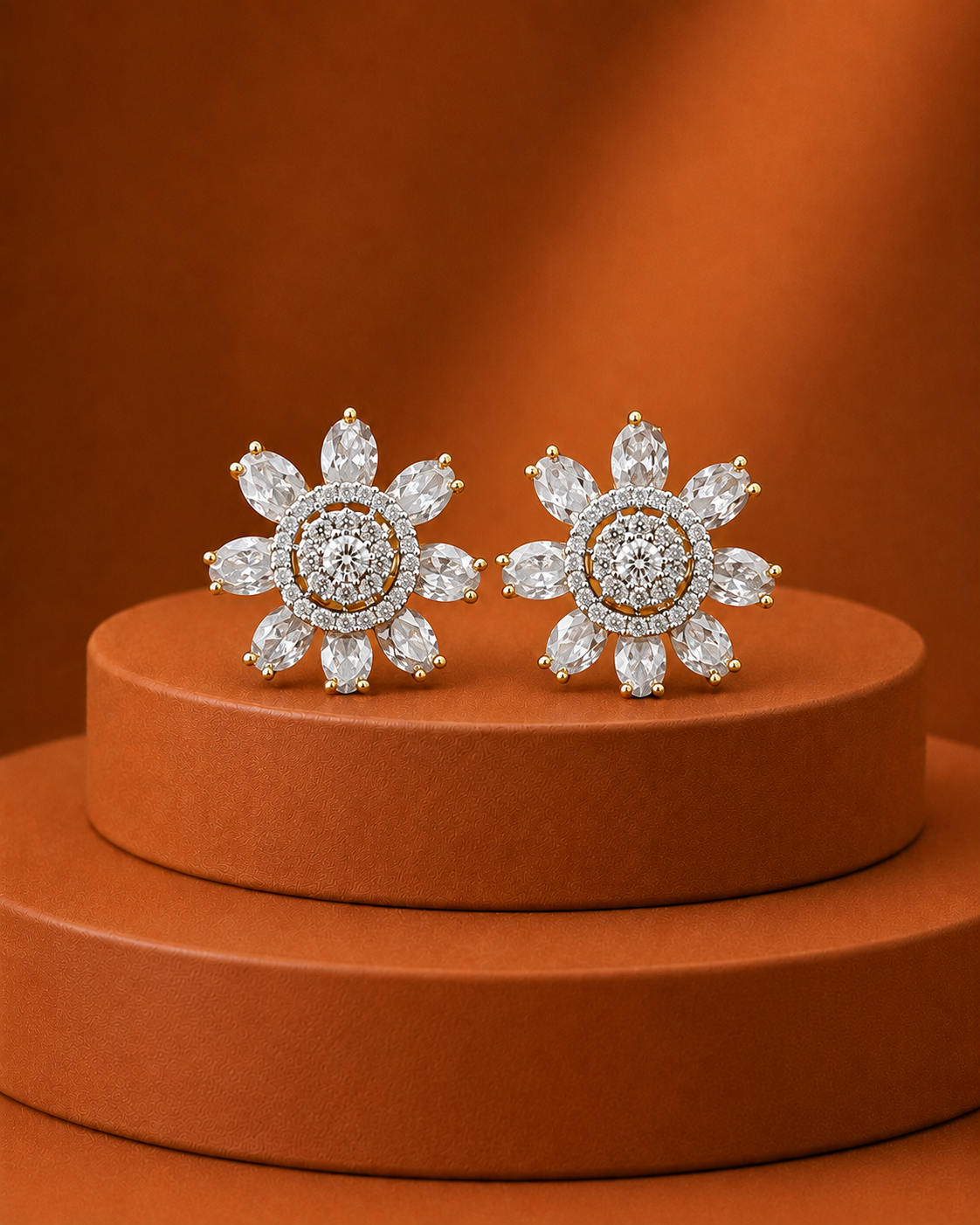 A pair of flower-shaped stud earrings with clear gemstones in a silver-toned setting, displayed on a round terracotta pedestal against a matching warm brown background.