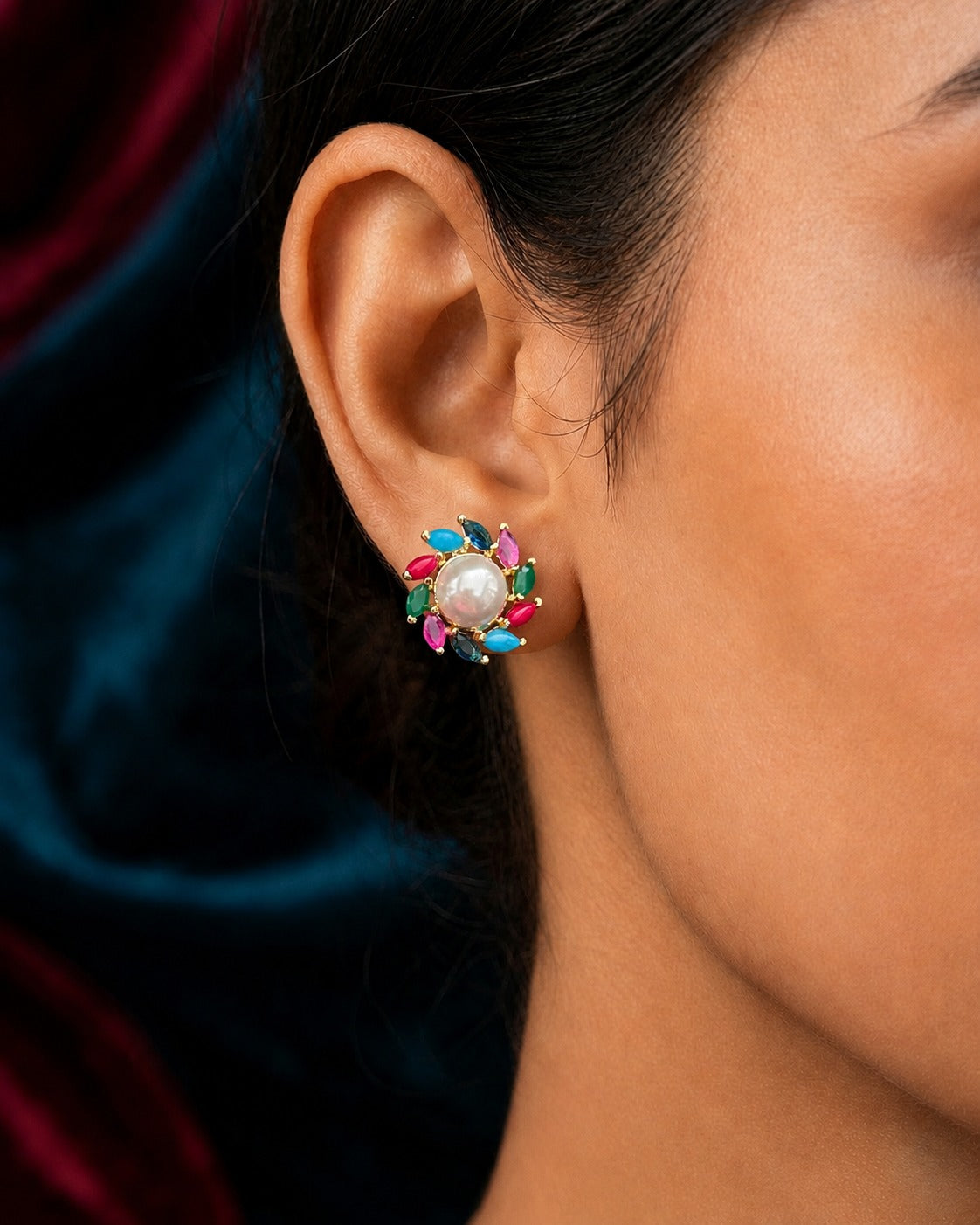 A close-up of a model's ear wearing a colorful stud earring with a white pearl center and small pink, blue, and green accents.