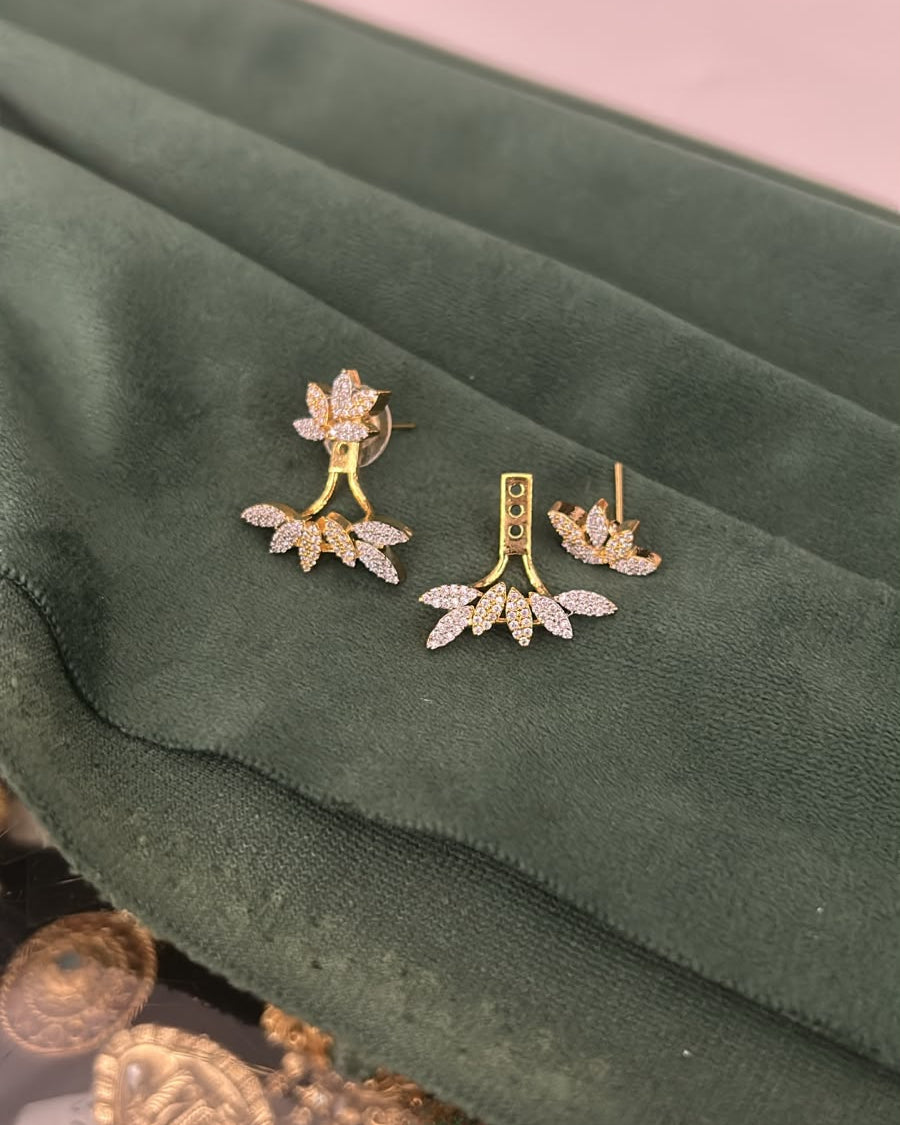 A pair of gold-toned floral and leaf stud earrings with clear rhinestone-like accents, displayed on a dark green velvet jewelry pouch.