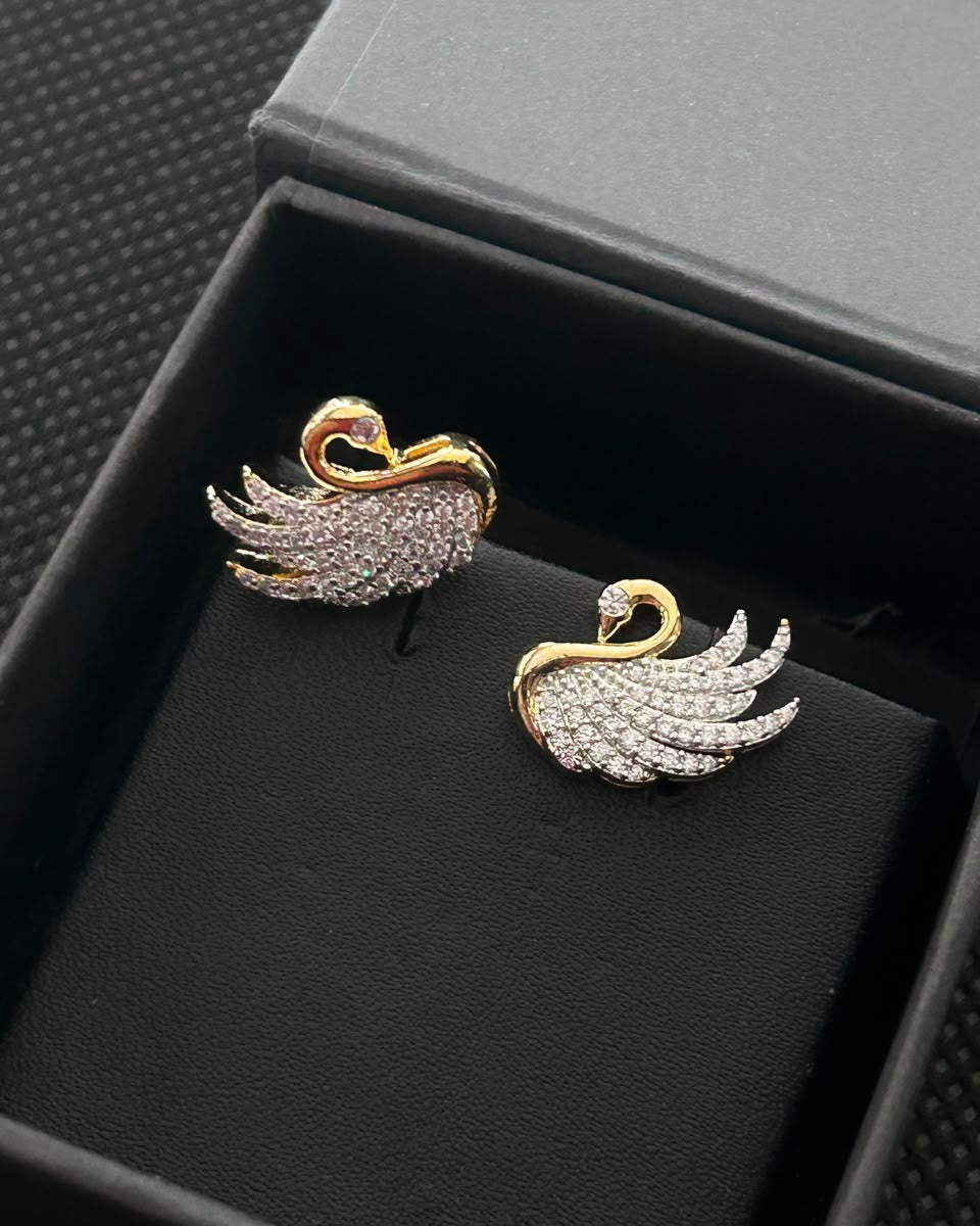 A pair of gold and crystal pavé swan stud earrings displayed on a black jewelry box.