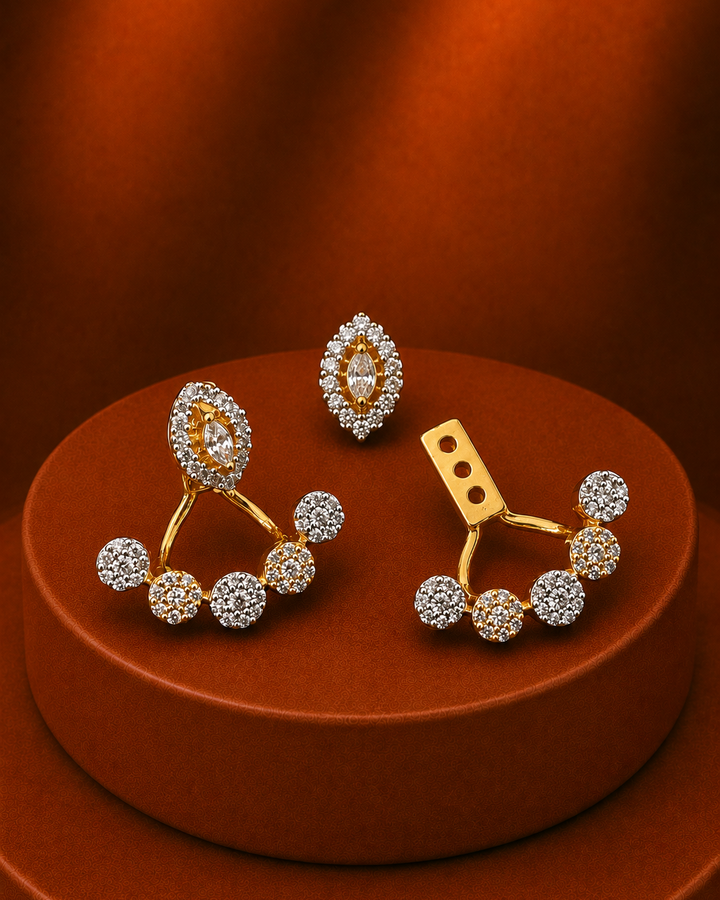 A pair of gold and crystal stud earrings displayed on a round brown pedestal against a warm brown background. The earrings feature gold-toned metal settings with multiple clear crystals, including oval and round stone clusters.