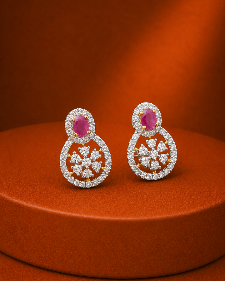 A pair of gold and diamond drop earrings with oval pink gemstones, displayed on a round orange pedestal against a matching orange background.