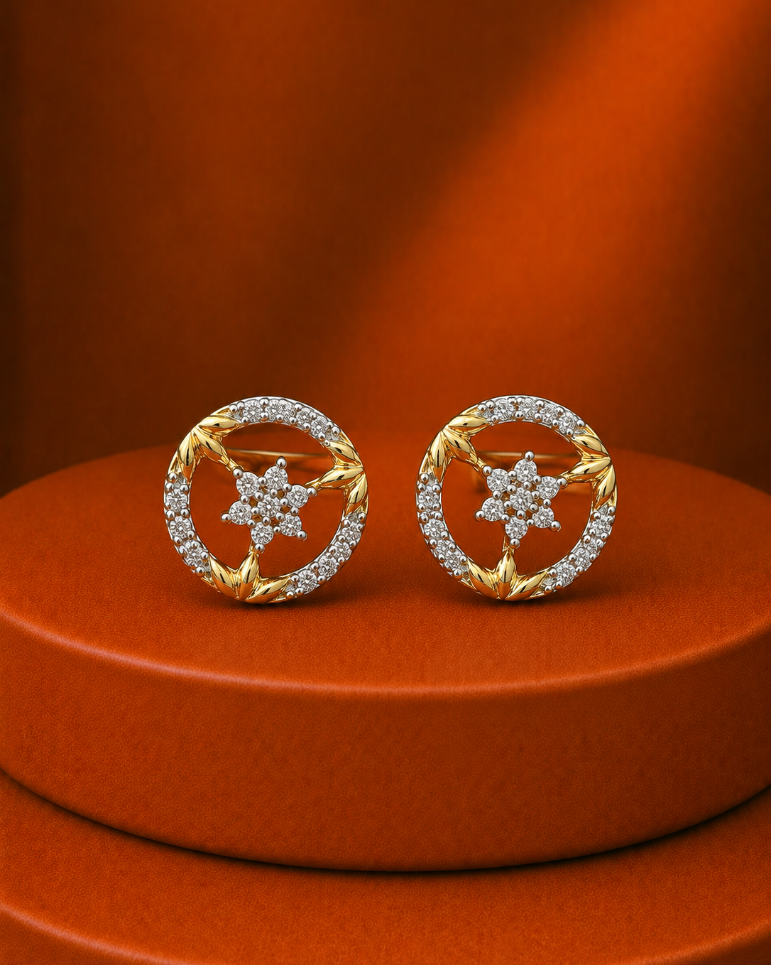 A pair of gold and diamond stud earrings displayed on a round orange pedestal against a matching orange background.