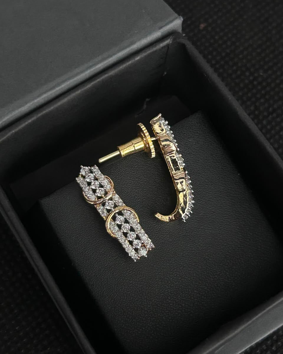 A pair of gold and silver-toned hoop earrings with pavé-set clear stones, displayed inside an open black jewelry box on a black cushion.