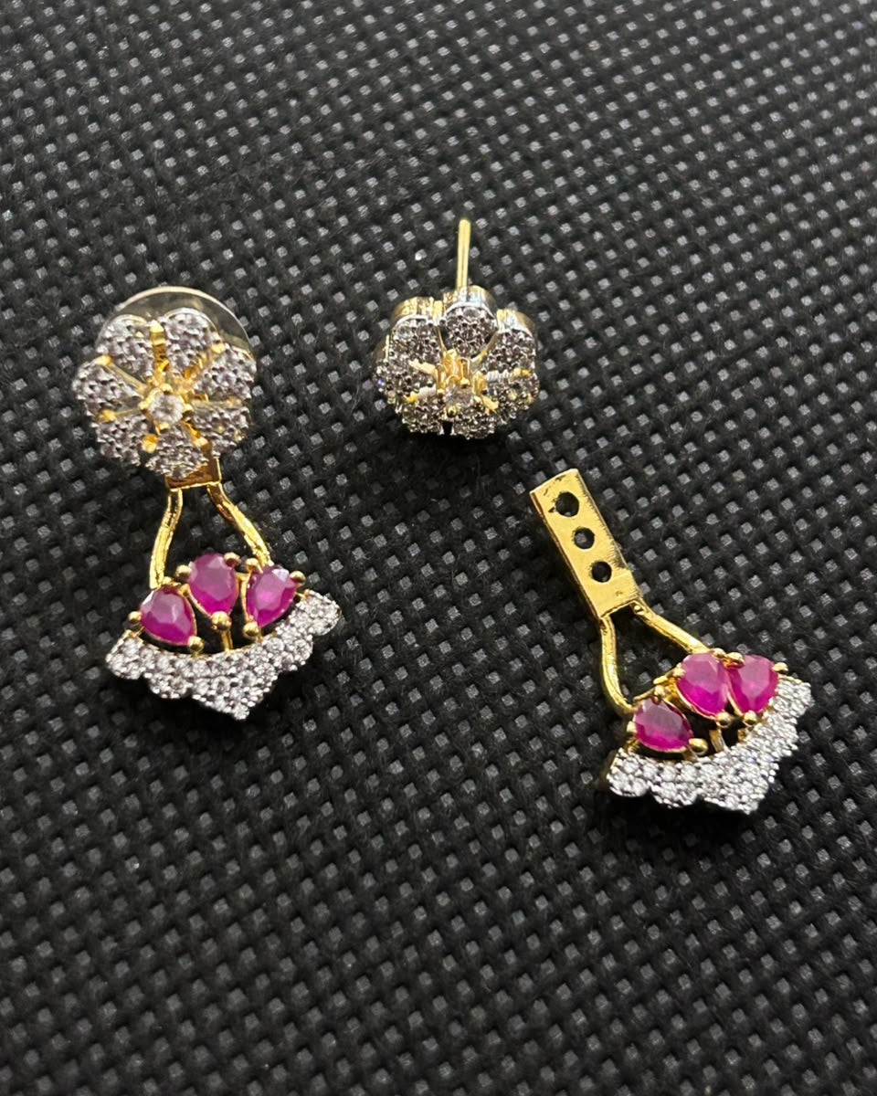 A pair of gold and silver floral drop earrings with pink gemstone accents, displayed on a textured black background.