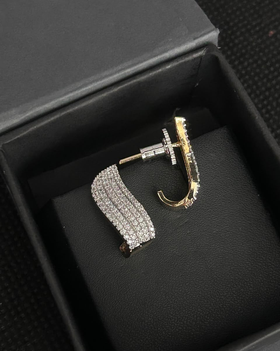 A pair of gold and silver huggie hoop earrings, one with a silver pavé band and the other with a gold pavé band, displayed inside a black jewelry box.