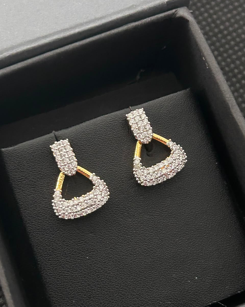 A pair of gold and silver pavé drop earrings displayed on a black textured jewelry box.