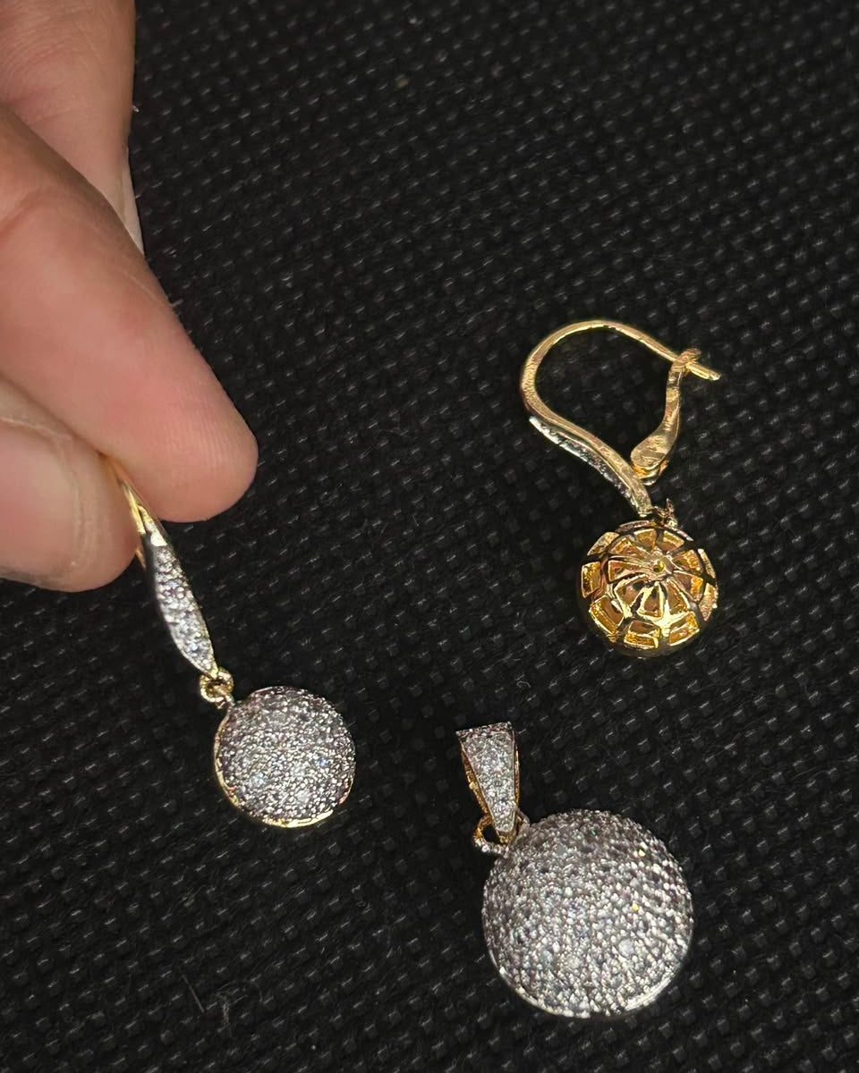 A pair of gold and silver pavé drop earrings displayed on a black textured background, with a hand holding one earring to show scale.