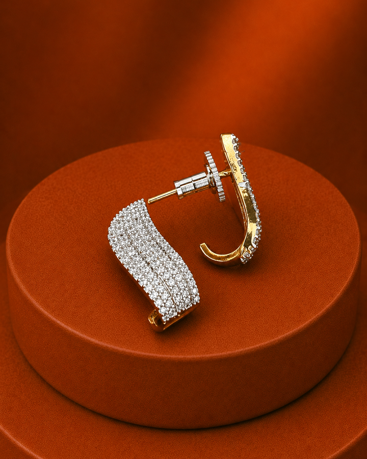 A pair of gold and silver pavé hoop earrings displayed on a round brown pedestal against a warm brown background.