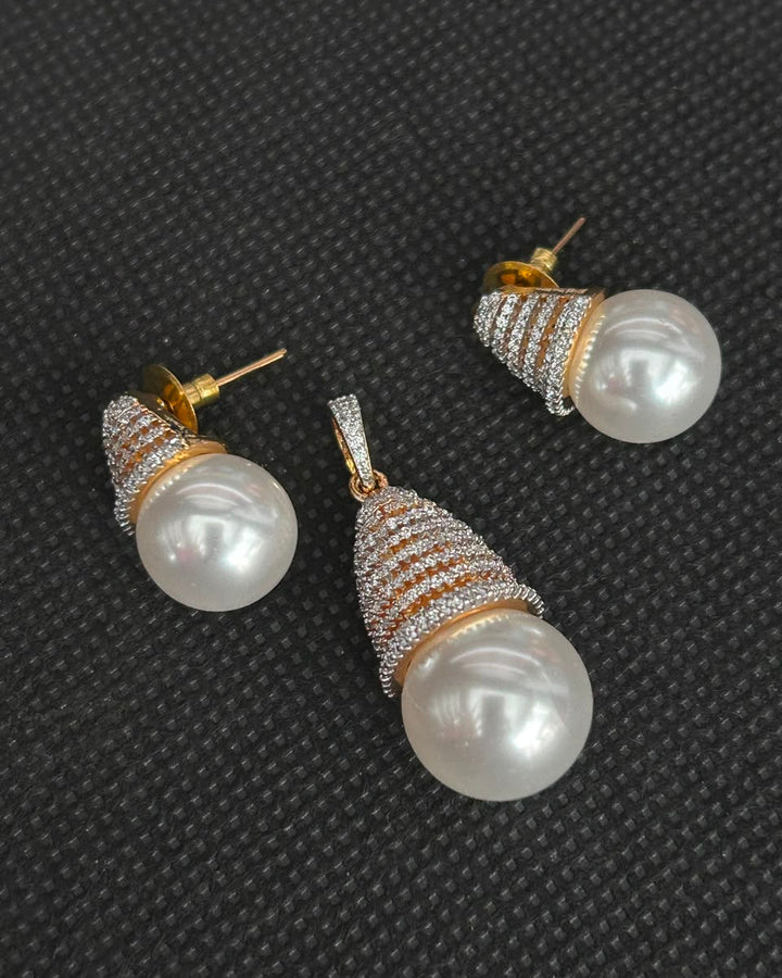 A pair of gold and white pearl drop earrings with pavé-set clear stones, displayed on a textured black background.