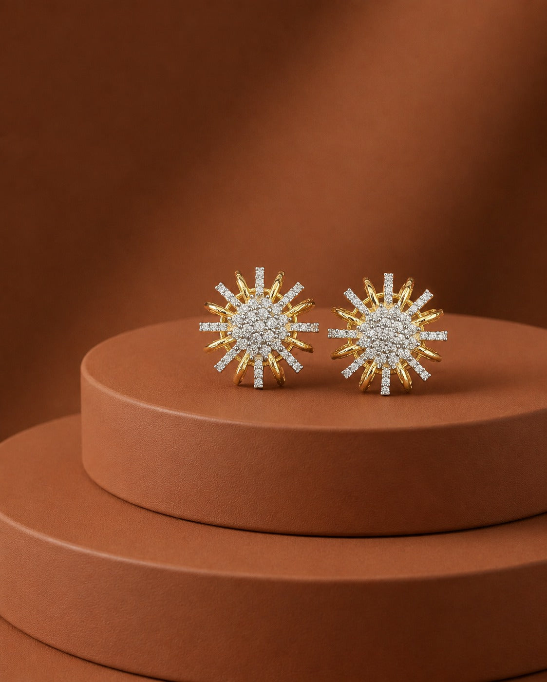 A pair of gold and white stone sunburst stud earrings displayed on a round terracotta pedestal against a matching warm brown background.