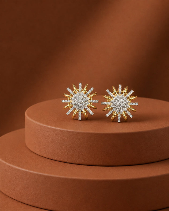 A pair of gold and white stone sunburst stud earrings displayed on a round terracotta pedestal against a matching warm brown background.