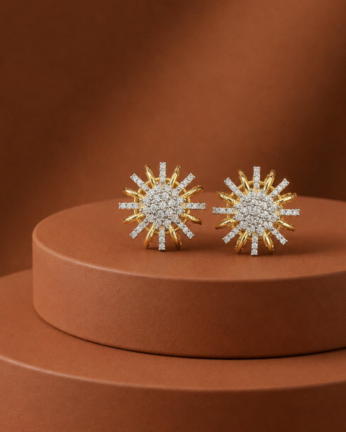 A pair of gold and white stone sunburst stud earrings displayed on a round terracotta pedestal against a matching warm brown background.