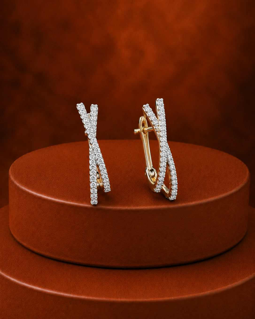 A pair of gold hoop earrings with pavé-set clear stones, arranged on a round brown display pedestal against a textured brown background.