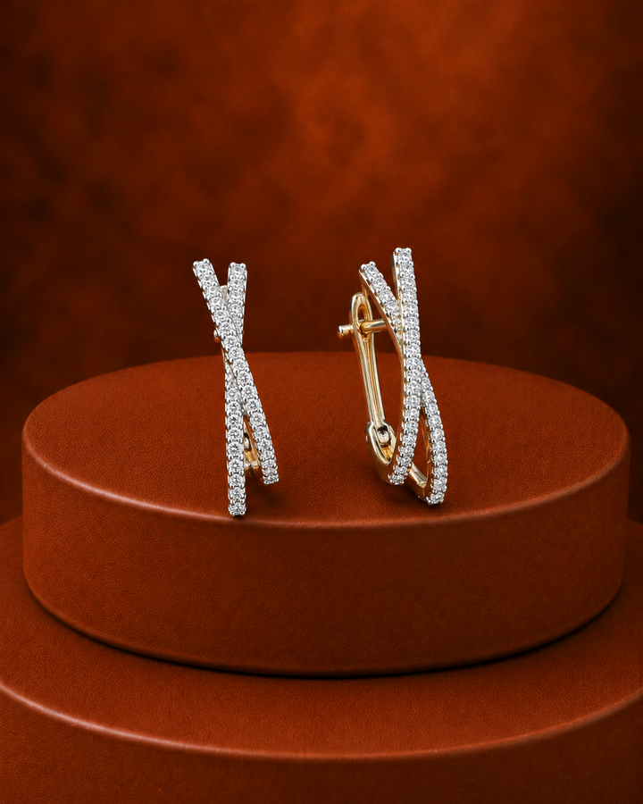 A pair of gold hoop earrings with pavé-set clear stones, arranged on a round brown display pedestal against a textured brown background.