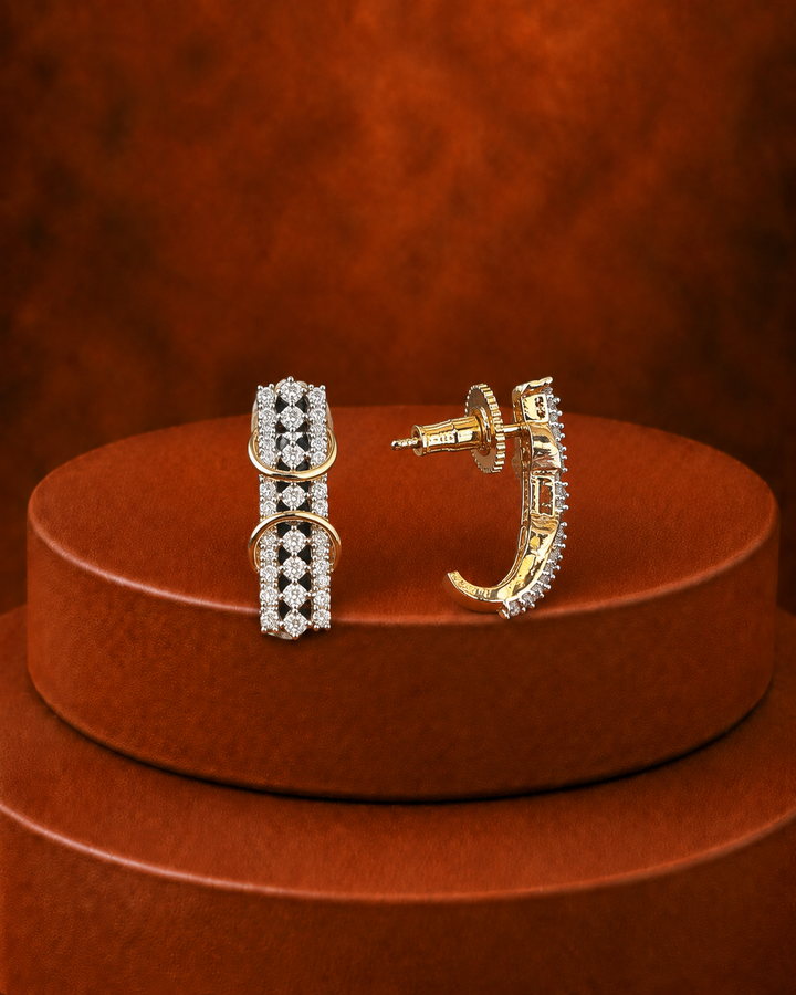 A pair of gold hoop earrings with rows of clear pavé-set stones, displayed on a round brown pedestal against a textured brown background.