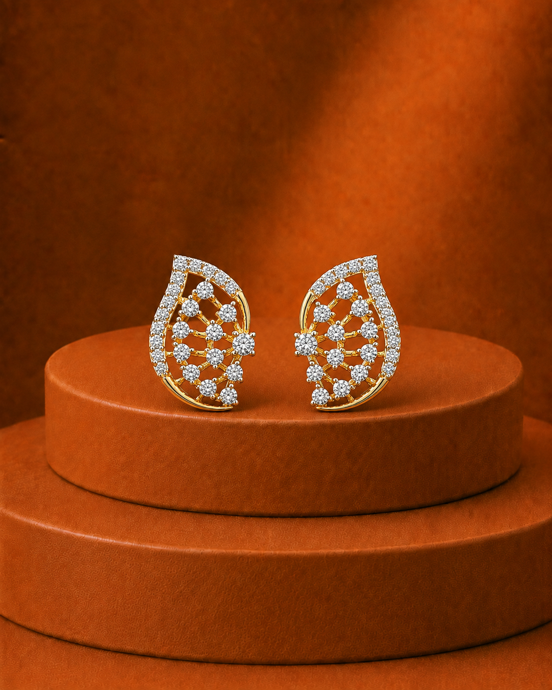 A pair of gold teardrop-shaped earrings set with clear pavé gemstones, displayed on a round brown pedestal against a matching brown background.