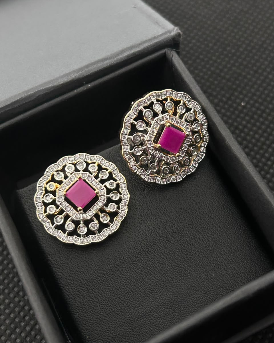 A pair of ornate silver-toned earrings with bright pink square center stones and surrounding clear stones, displayed inside a black jewelry box.