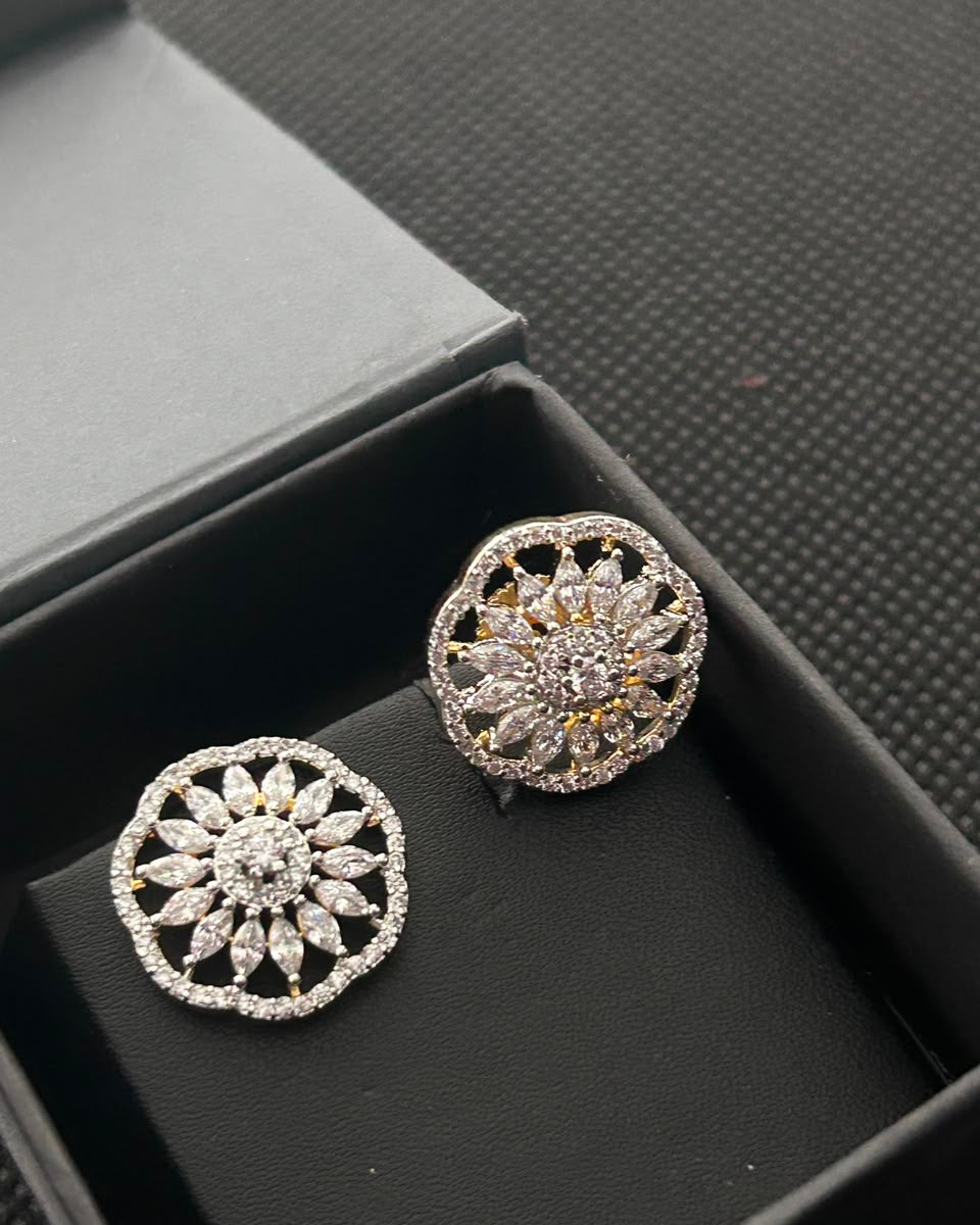 A pair of round floral stud earrings with intricate filigree and pave-set clear stones, displayed inside an open black jewelry box.