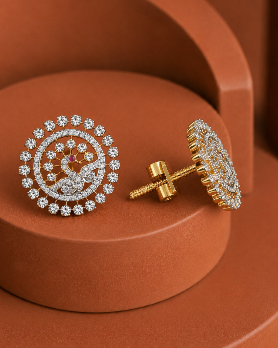 A pair of round gold and white-metal stud earrings adorned with clear stones, displayed on terracotta-colored geometric pedestals. One earring is shown from the front, featuring a circular halo design with a central floral motif, while the other is shown from the side, displaying the gold post and butterfly back.
