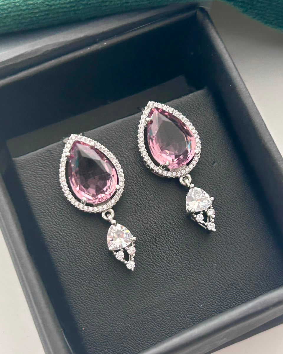 A pair of silver-tone drop earrings with large pink teardrop-shaped gemstones and small clear stones, displayed in a black jewelry box.