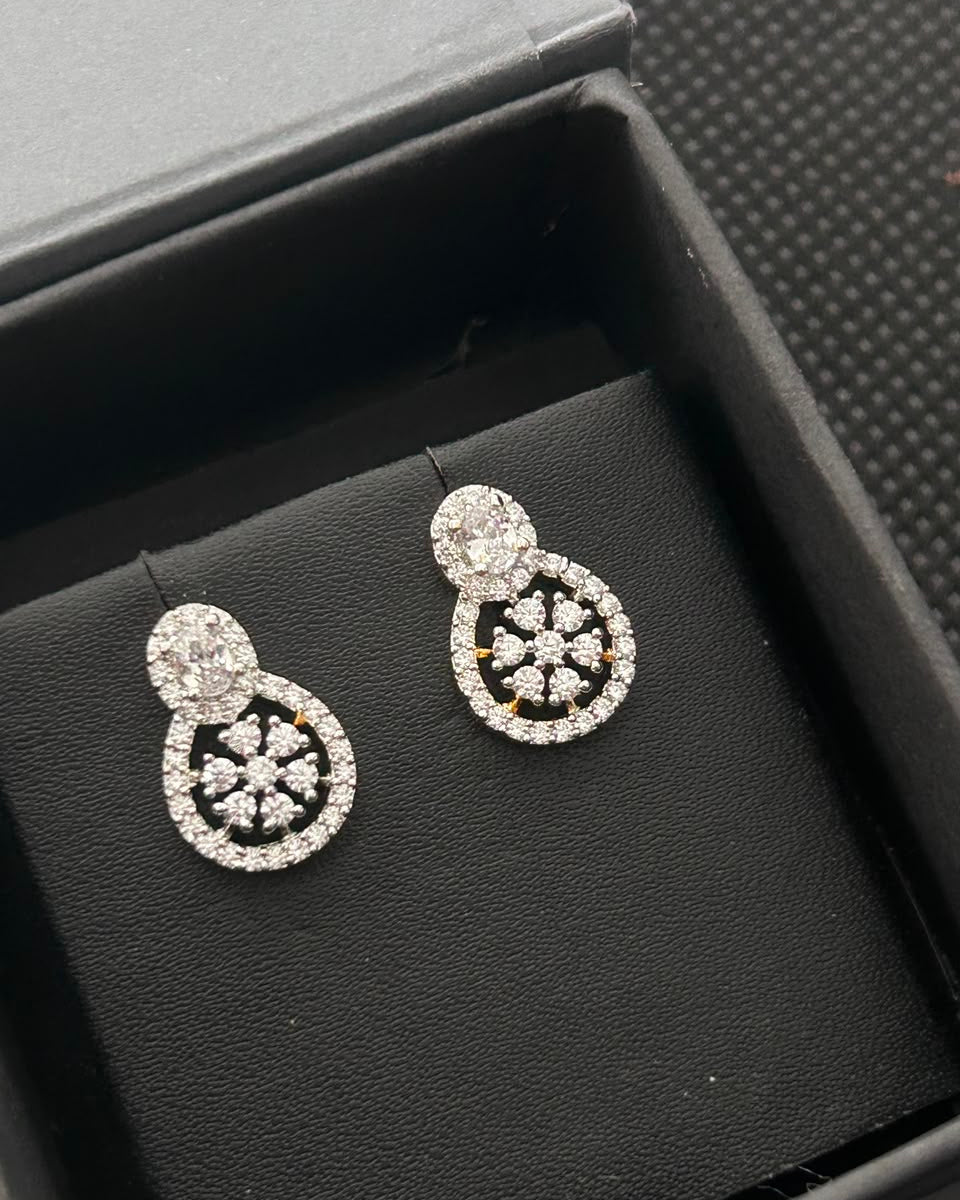 A pair of silver-toned drop earrings with circular pavé crystal designs, displayed inside a black jewelry box.