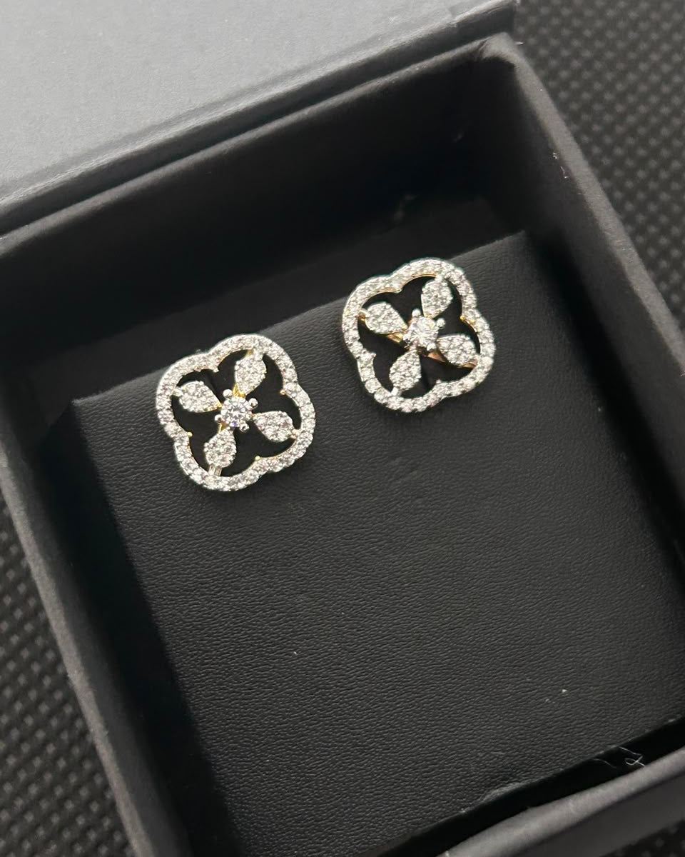A pair of silver-toned stud earrings with a floral clover design set with small clear stones, displayed on a black velvet insert inside a black jewelry box.