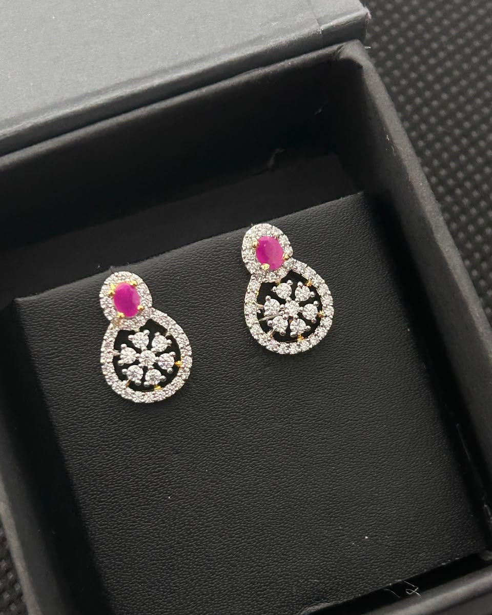A pair of silver-toned teardrop-shaped earrings with a bright pink oval center stone and a surrounding halo of small clear stones, displayed on a black velvet insert inside a black jewelry box.