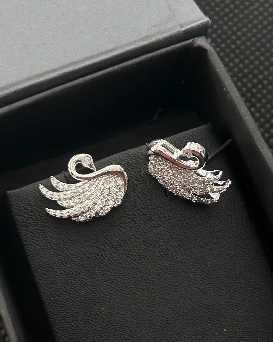 A pair of silver-toned swan-shaped stud earrings covered in small clear stones, displayed inside a black jewelry box.
