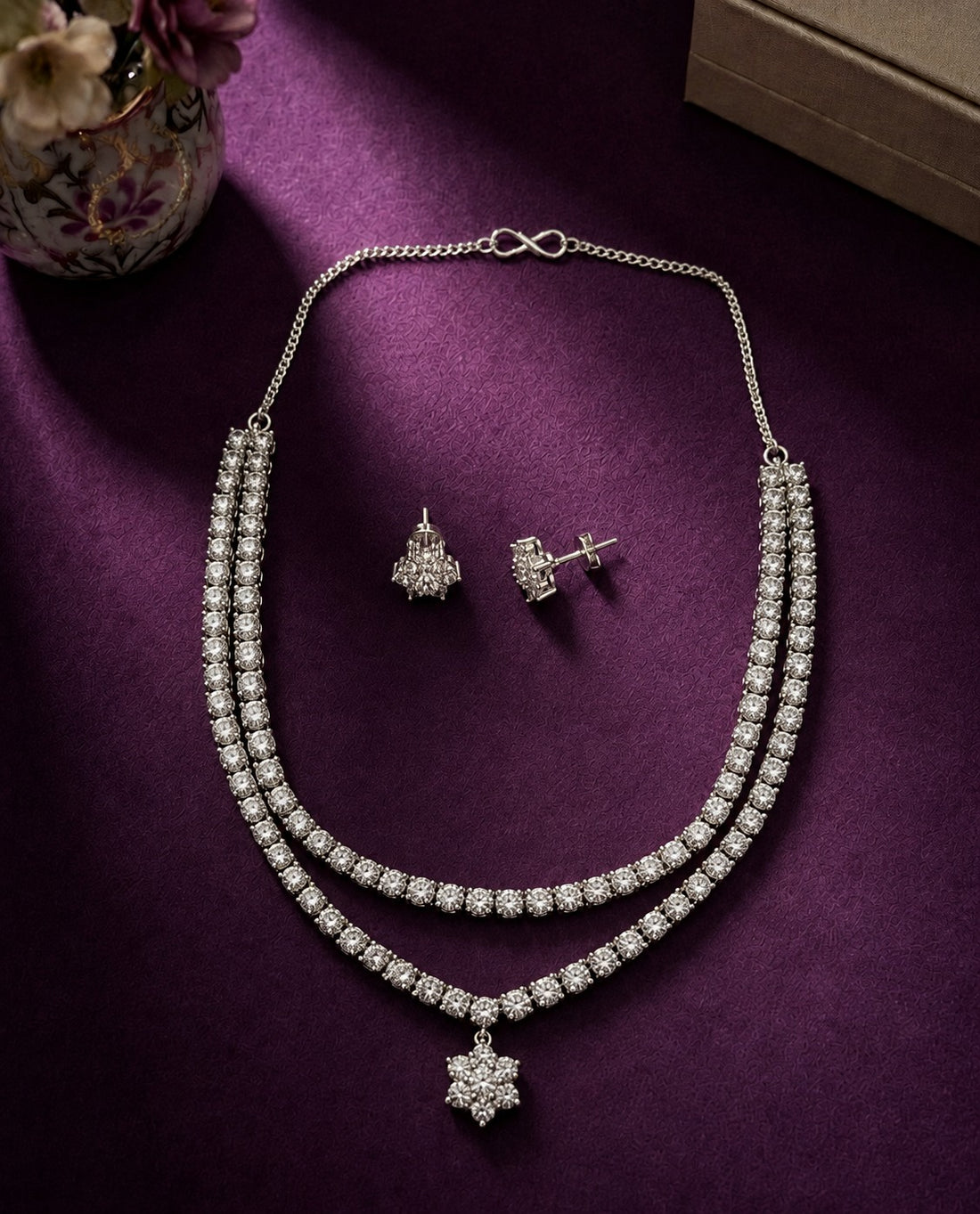A silver-tone double-strand necklace with a matching star-shaped pendant and matching stud earrings, displayed on a deep purple satin fabric background.