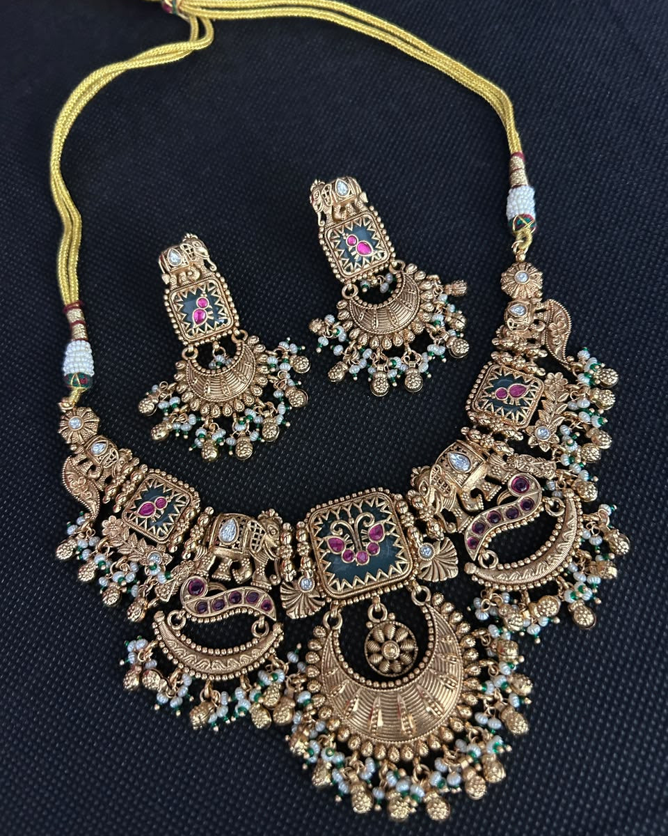 An ornate gold-toned traditional necklace with matching earrings, decorated with colorful enamel details and small bead accents, displayed on a dark textured background.
