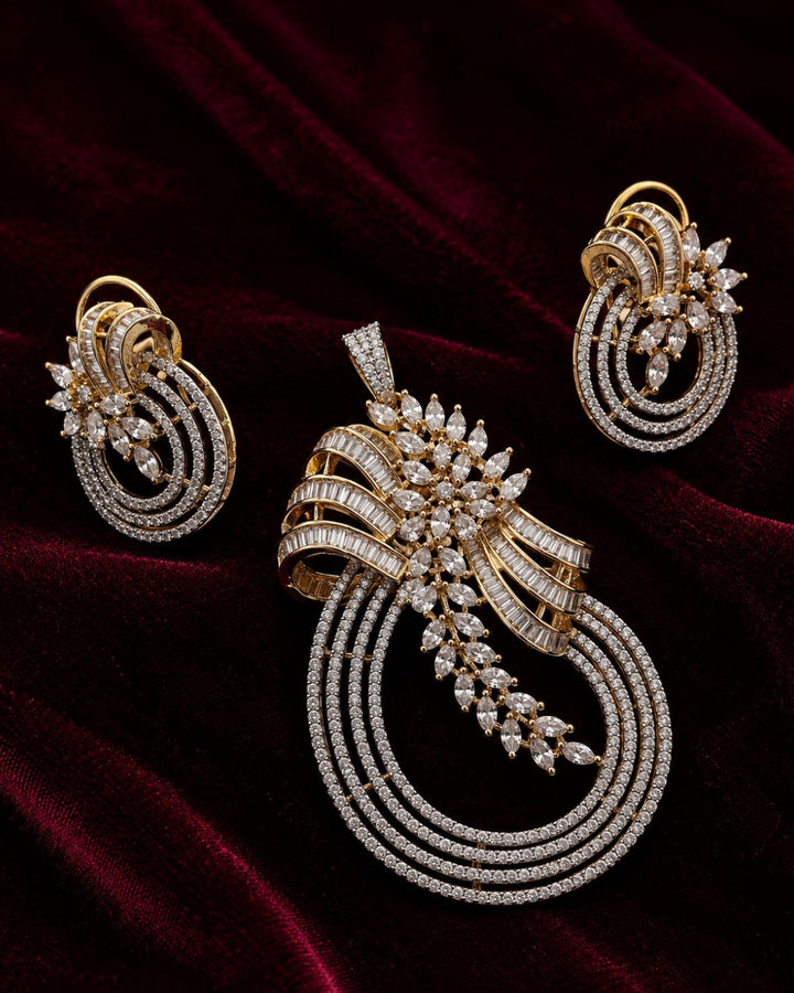 An ornate gold jewelry set featuring a large pendant, matching earrings, and a slim bracelet, all adorned with sparkling clear stones and set against a dark red velvet background.