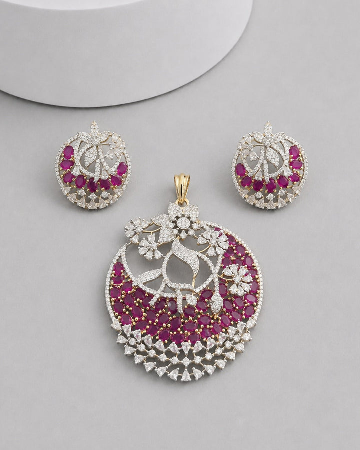 An ornate jewelry set featuring a large crescent-shaped pendant, a matching pair of round earrings, and a small gold clasp, all decorated with white stones and deep pink gemstones on a light gray background.