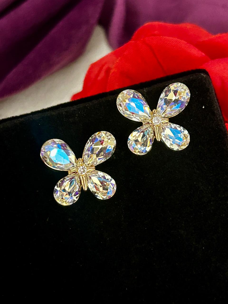 Butterfly-shaped earrings with crystal-like stones on a black background