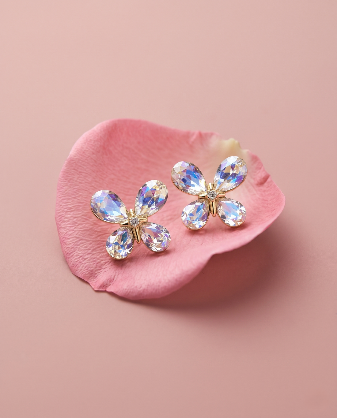 Butterfly-shaped earrings with crystal details on a pink petal against a pink background