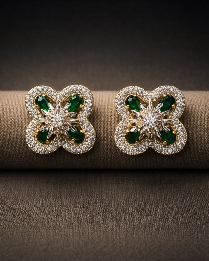 Butterfly-shaped earrings with green gemstones and gold accents on a brown surface.