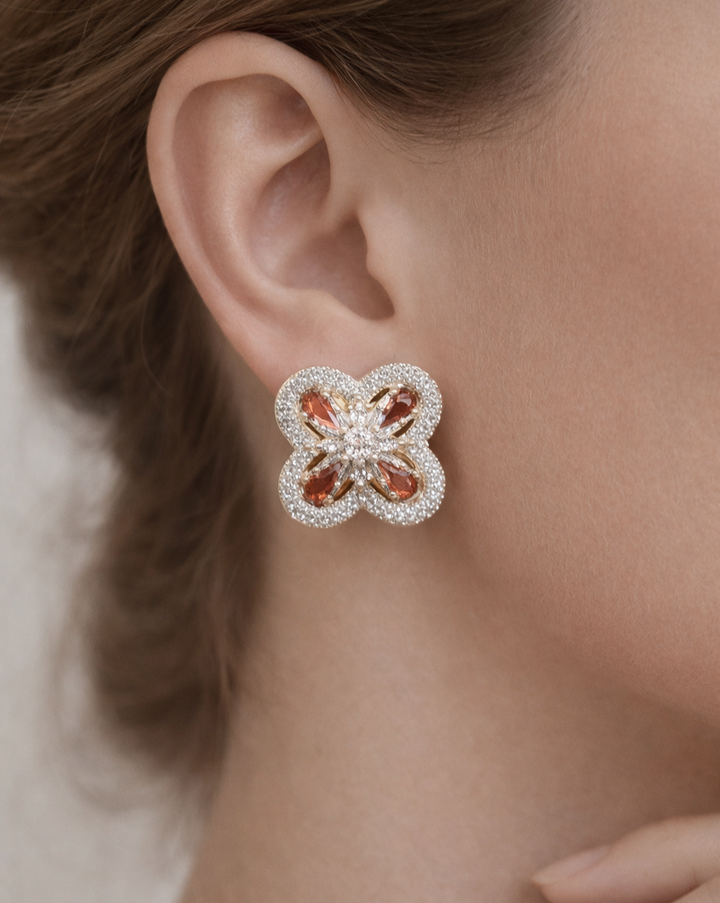 Close-up of a person wearing a floral earring with pink stones and clear accents.