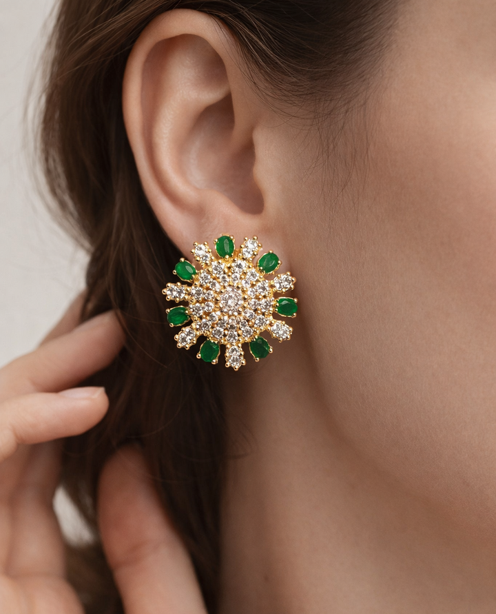 Close-up of a person wearing a gold earring with green gemstones.
