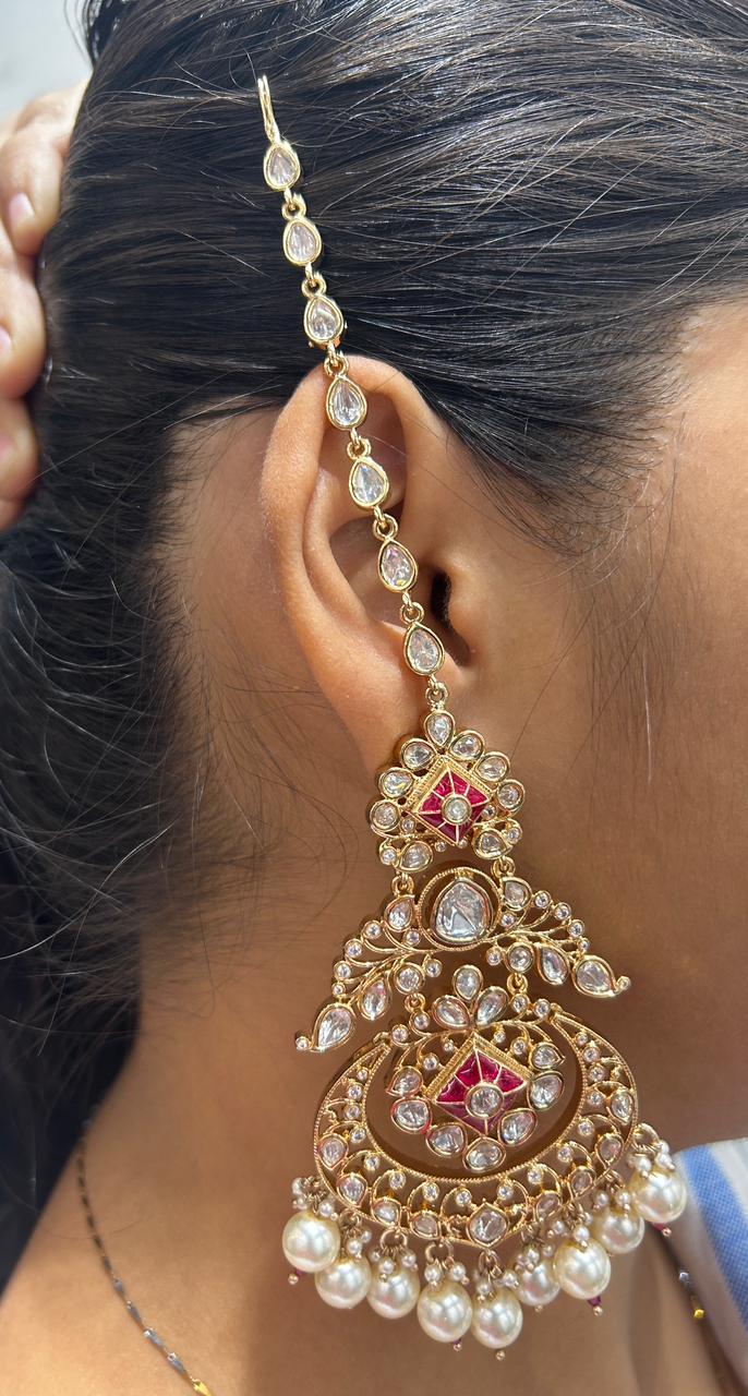 Close-up of a person wearing an ornate gold earring with pearls and gemstones.