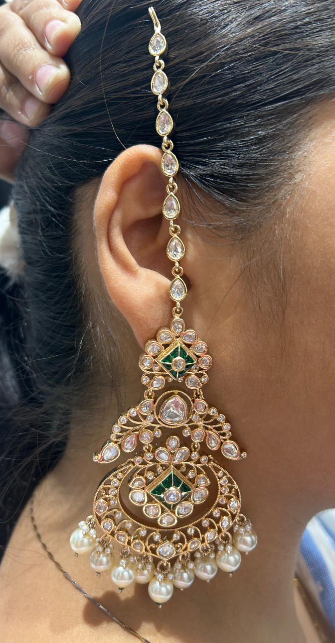 Close-up of a person wearing an ornate gold earring with pearls and green gemstones.