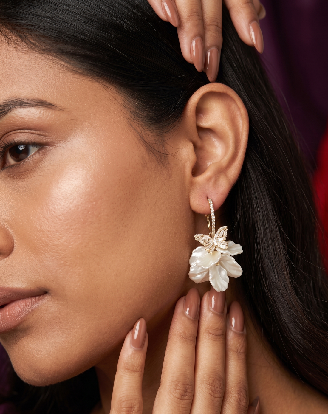 Close-up of a woman wearing a floral earring with one hand adjusting her hair.