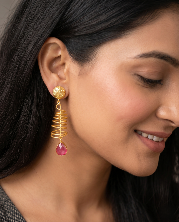 Close-up of a woman wearing gold earrings with a pink gemstone.